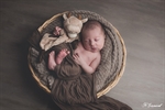Photogaphie d'un nouveau né qui dort dans une corbeille en osier avec son doudou tons marron réalisée par noelle gamand photographe nouveau né avignon vaucluse